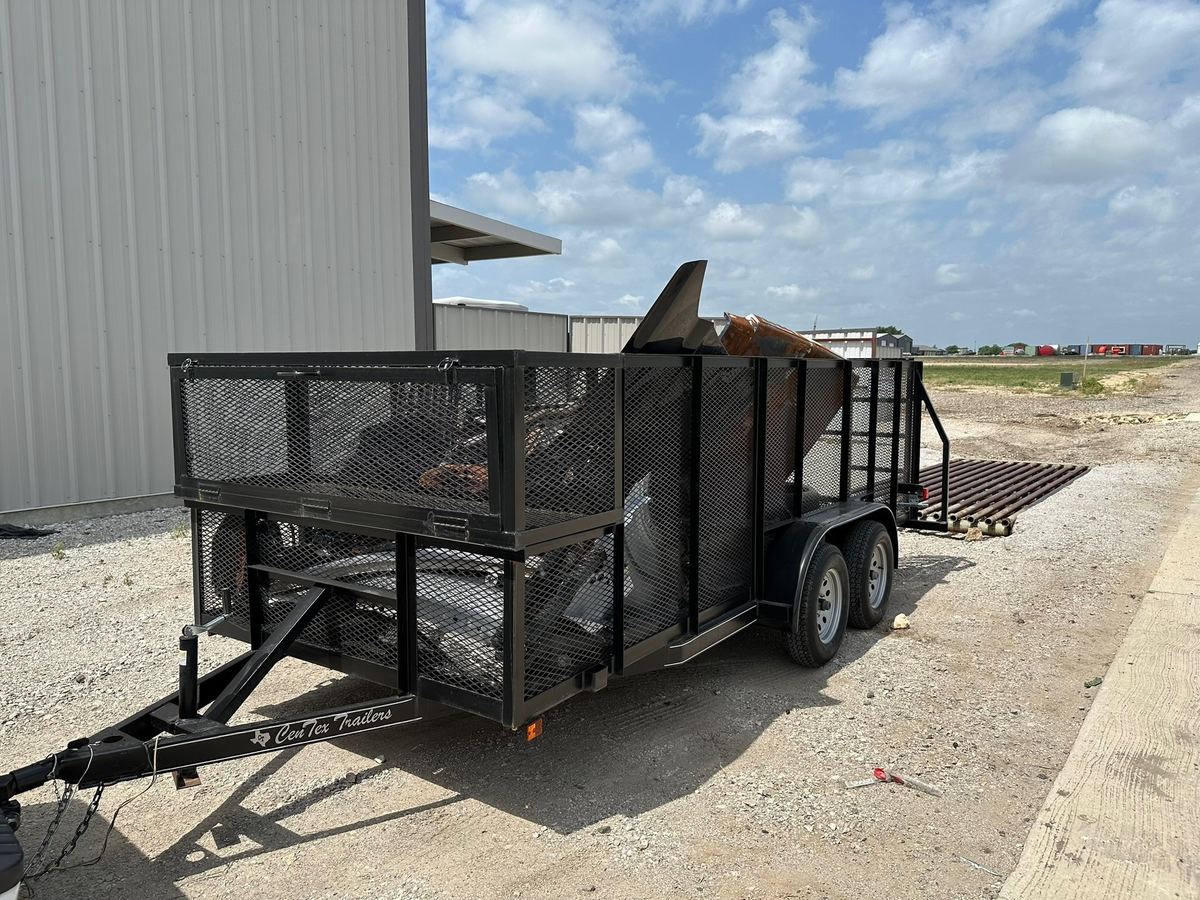 Open-top mesh hauling trailer loaded with scrap metal and debris