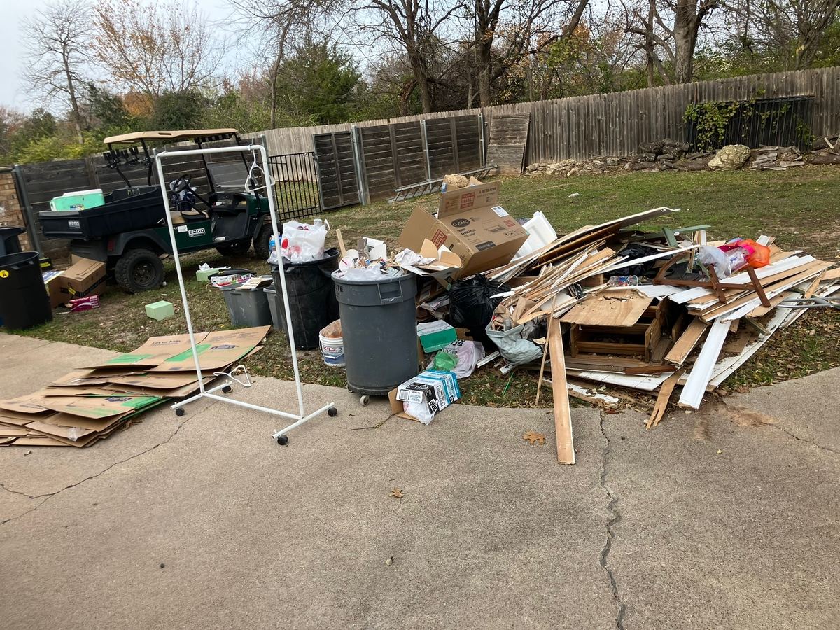 Pile of old lumber, trim boards, cardboard and trash cans on a driveway