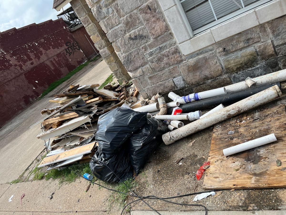Pile of lumber, drywall scraps, PVC pipe and trash bags beside a stone house