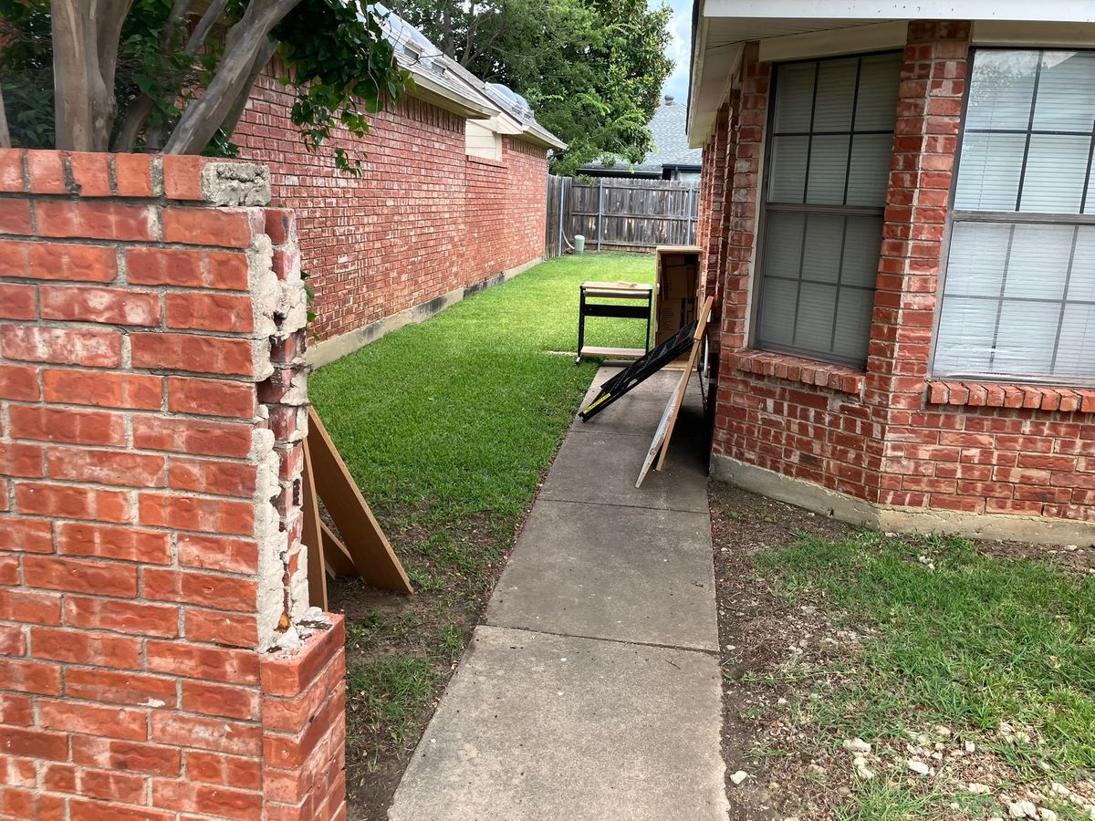 Boards, a workbench and boxes along a brick side yard walkway