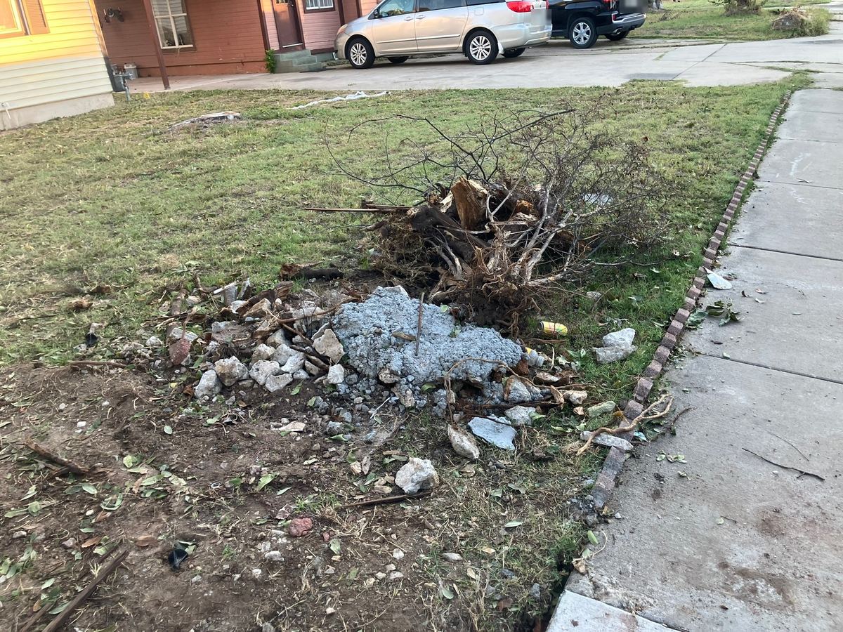 Uprooted tree stump, roots and broken concrete piled on a front lawn