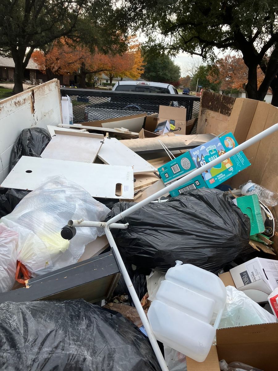 Old shelving boards, trash bags and cardboard boxes piled in a truck bed with a trailer behind it