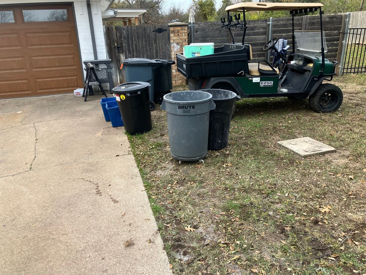 Backyard driveway and lawn cleared after debris haul-away, with trash cans and a golf cart left in place